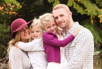Trent Moen with his wife and their two young daughters, outdoors in autumn.